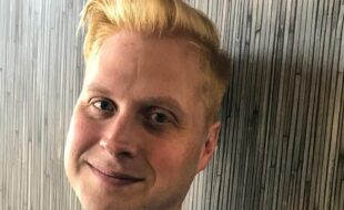 A man, a close up of his face, leaning against a wall, smiling