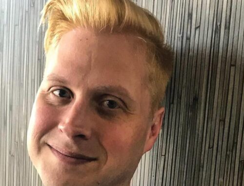 A man, a close up of his face, leaning against a wall, smiling