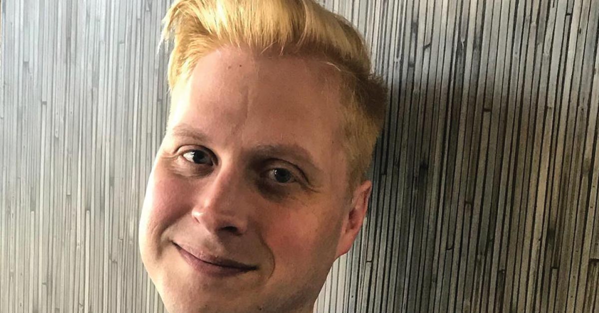 A man, a close up of his face, leaning against a wall, smiling